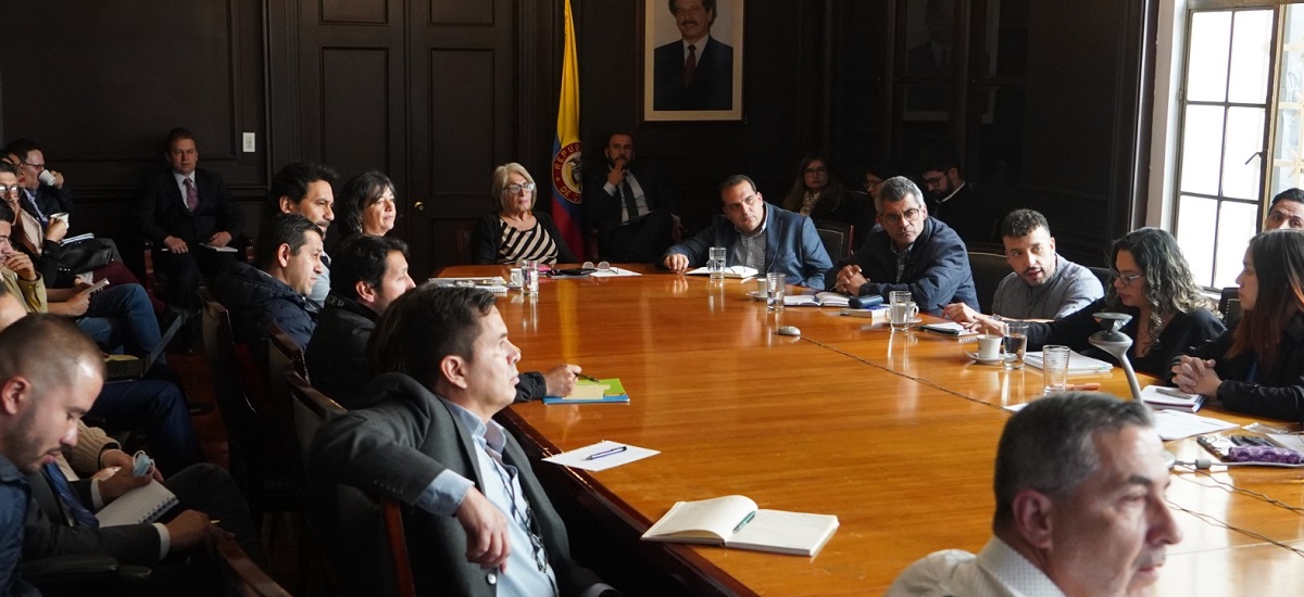 En la imagen se puede ver a la Ministra en una reunión, rodeada de un grupo de personas, se nota un ambiente de concentración en el que parece discuten de un tema muy importante