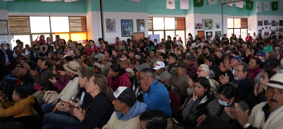 en la imagen se puede apreciar un grupo de personas, en su mayoria campesinos, en lo que parece ser una conferencia, se puede apreciar como la mayoria esta aplaudiendo, de fondo, se pueden apreciar algunos cuadros en las paredes 
