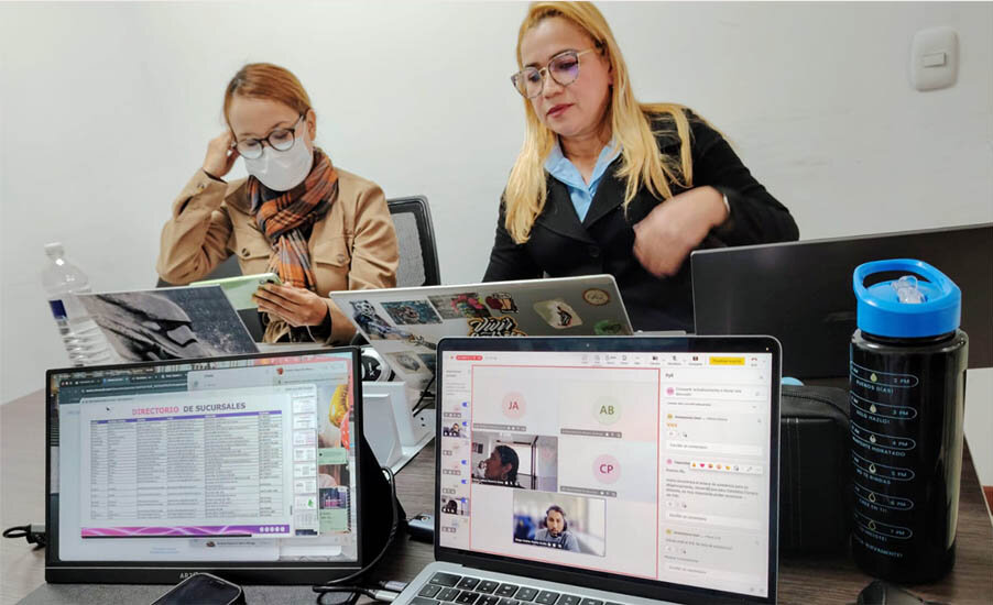 Dos personas están sentadas en una mesa con sus portátiles abiertos y varios documentos.