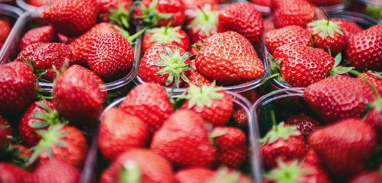 La imagen muestra un gran expositor de fresas frescas, con varios recipientes llenos de esta fruta roja. Las fresas están dispuestas de forma atractiva, mostrando su vibrante color y su atractivo aspecto. Los recipientes están colocados en distintas posiciones, algunos más cerca del primer plano y otros más atrás, creando una sensación de profundidad y abundancia.
