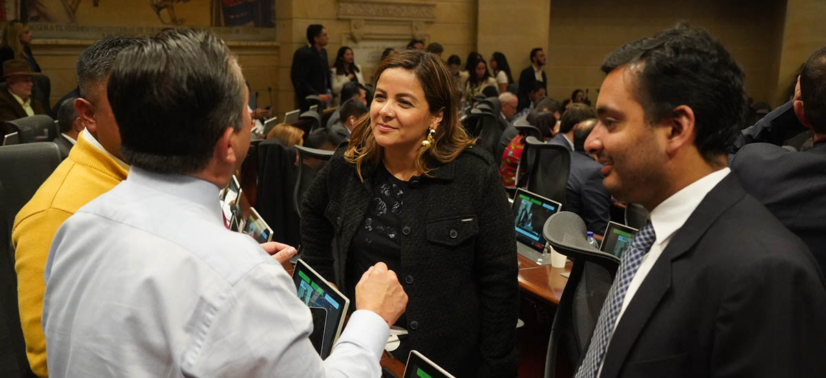 En la imagen se puede observar a la Ministra Jhenifer Mojica, dialogando con tres hombres, de fondo se puede observar a muchas personas reunidas, en lo que se ve una jornada laboral extensa