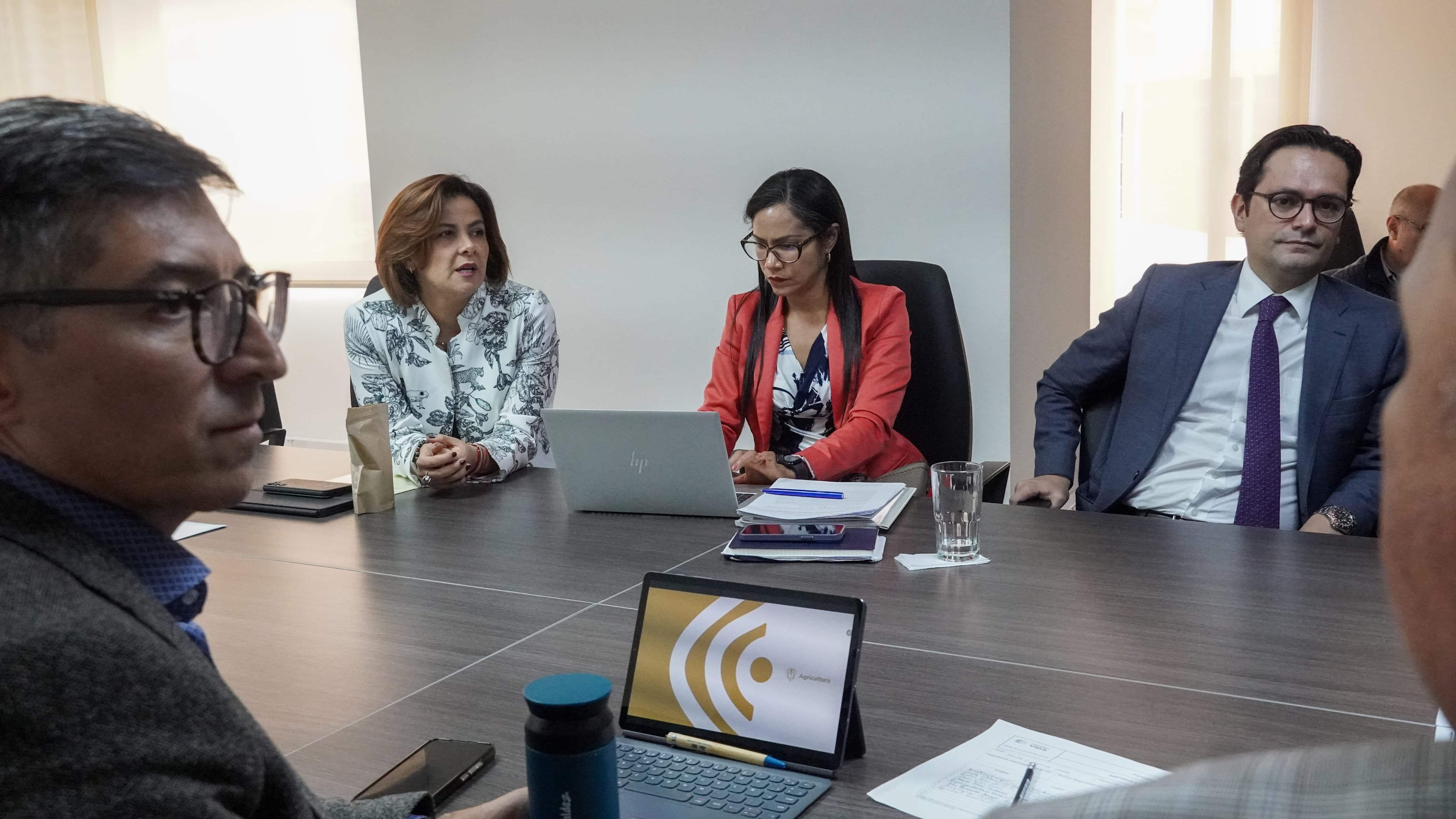En la imagen se puede ver un grupo de personas reunidas, vestidas de manera muy elegante, se puede apreciar que tienen portátiles y donde tomar notas.