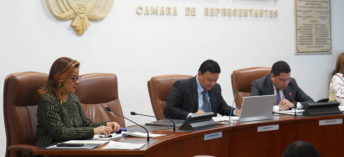 La imagen muestra a un grupo de personas sentadas en una sala de conferencias, participando en una reunión. Hay cuatro personas en la sala, dos de ellas sentadas en sillas junto a una mesa y las otras dos sentadas en un sofá. Cada persona tiene un ordenador portátil delante, lo que indica que están trabajando o discutiendo algo relacionado con su trabajo.