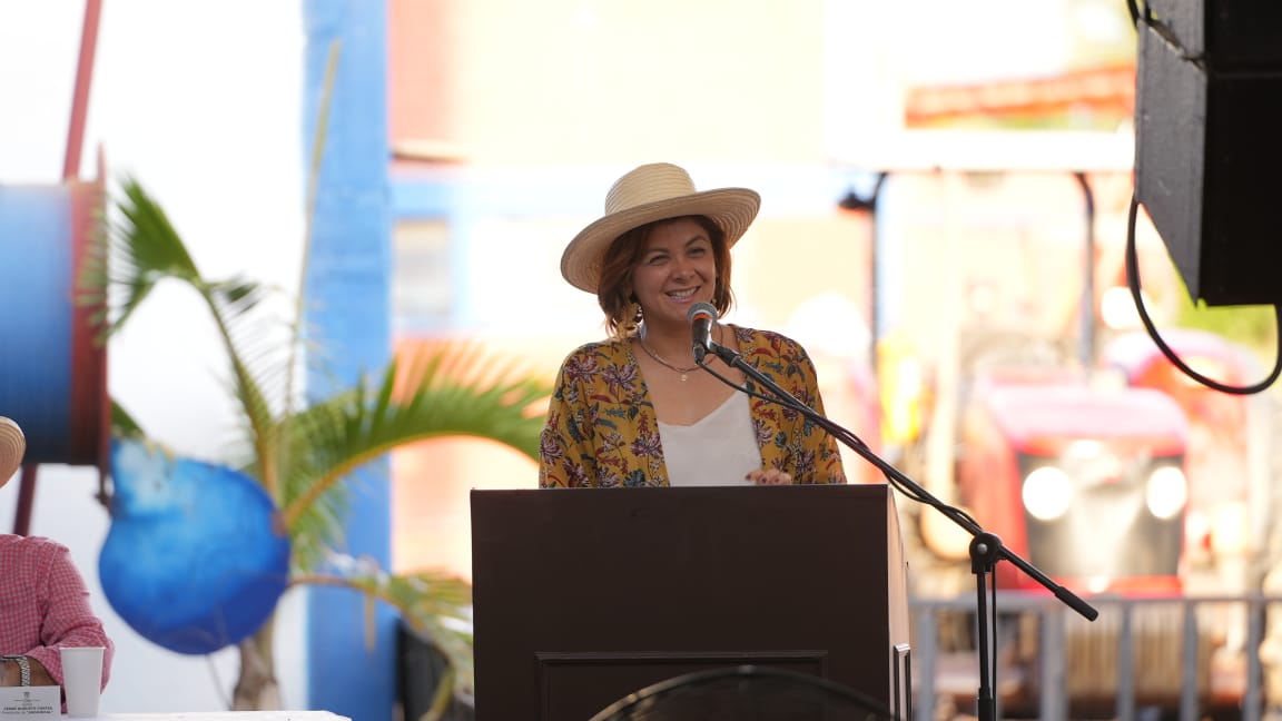En la imagen se puede ver a la ministra de agricultura Jhenifer Mojica en una conferencia al aire libre, se le ve muy contenta, sonriendo y apreciando el momento.