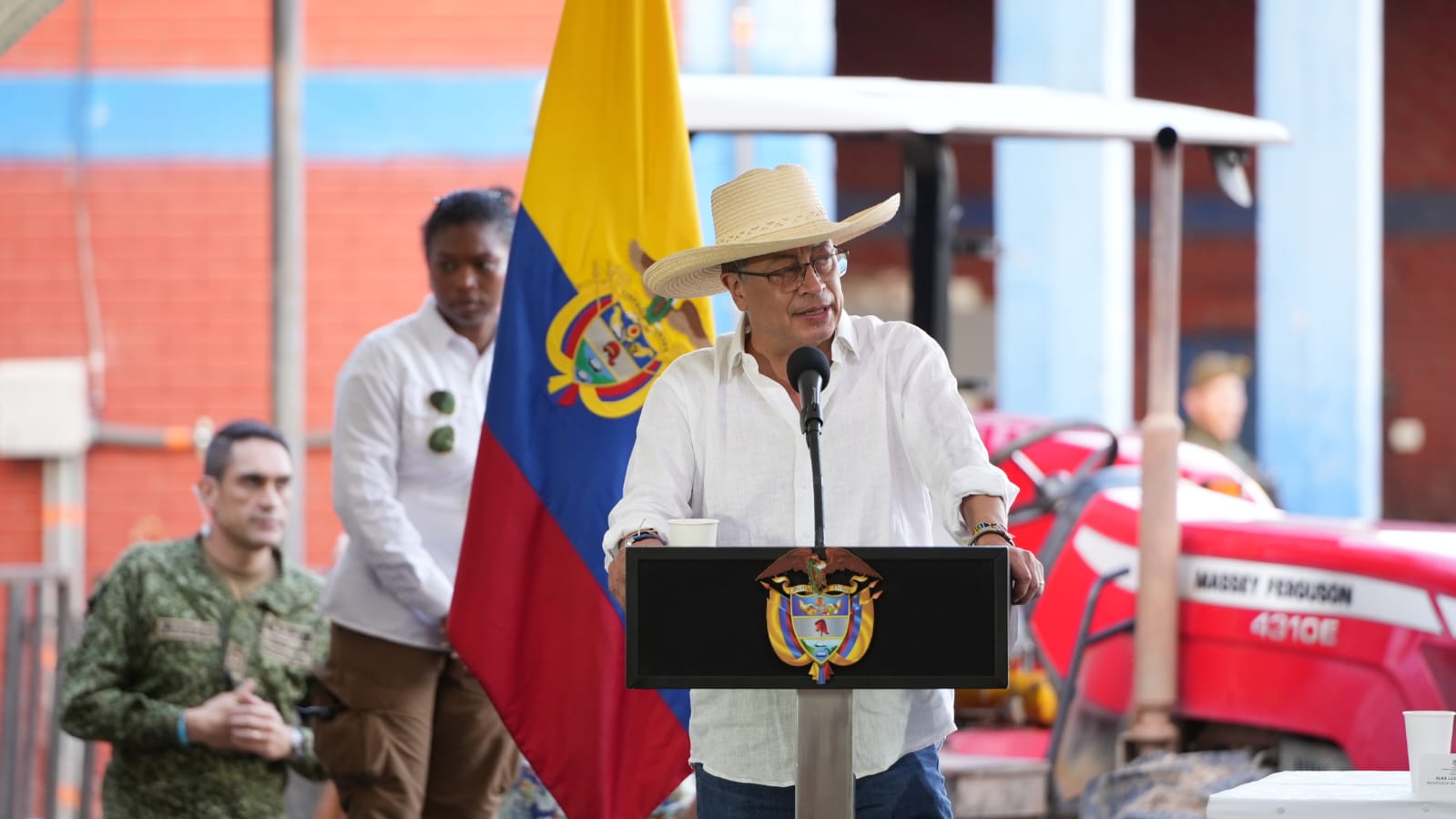 En la imagen se puede observar al presidente Gustavo Petro dando un discurso al publico, de fondo se puede apreciar la bandera de Colombia. 