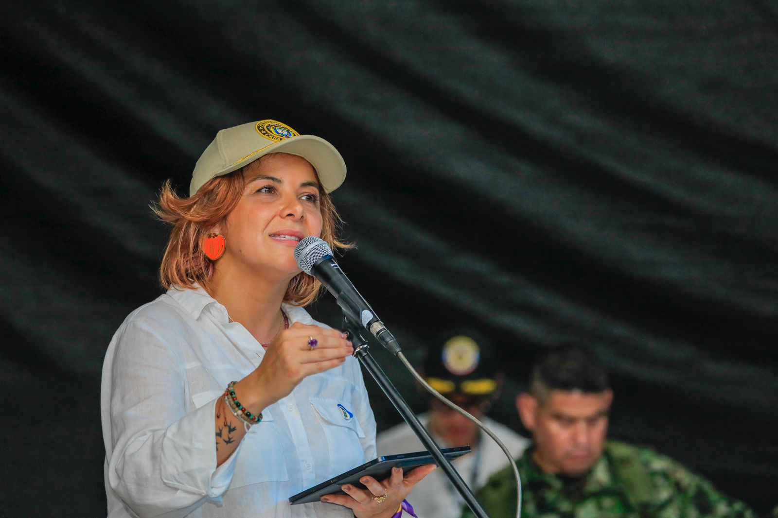 en la imagen se  puede ver a la ministra Jhenifer Mojica en una conferencia, hablando por un micrófono, en lo que parece un acto publico.