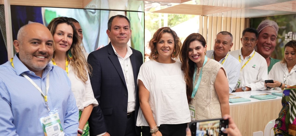 En la imagen se puede apreciar a la Ministra Jhenifer Mojica, la cual esta rodeada de varias personas, al parecer en un evento publico, , como sugiere el telón de fondo que incluye una gran pantalla que muestra lo que parece ser un logotipo o emblema, y una pancarta con texto que no es totalmente visible. El ambiente parece cordial y profesional, todos sonríen y miran hacia la cámara.