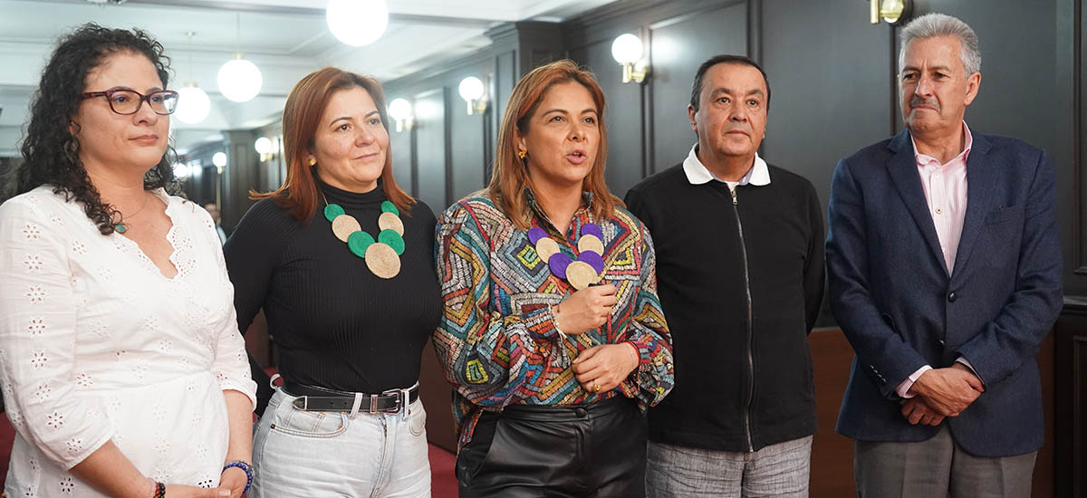 La imagen muestra a un grupo de cinco personas de pie unas junto a otras en una habitación. Parecen estar posando para una foto, y algunos de ellos llevan corbata. El grupo está formado por tres mujeres y dos hombres, todos vestidos de etiqueta. Las mujeres llevan vestidos, mientras que los hombres llevan trajes. Los individuos están en fila, con las mujeres a la izquierda y los hombres a la derecha. La sala en la que se encuentran tiene un ambiente formal, probablemente un tribunal o un entorno similar.
