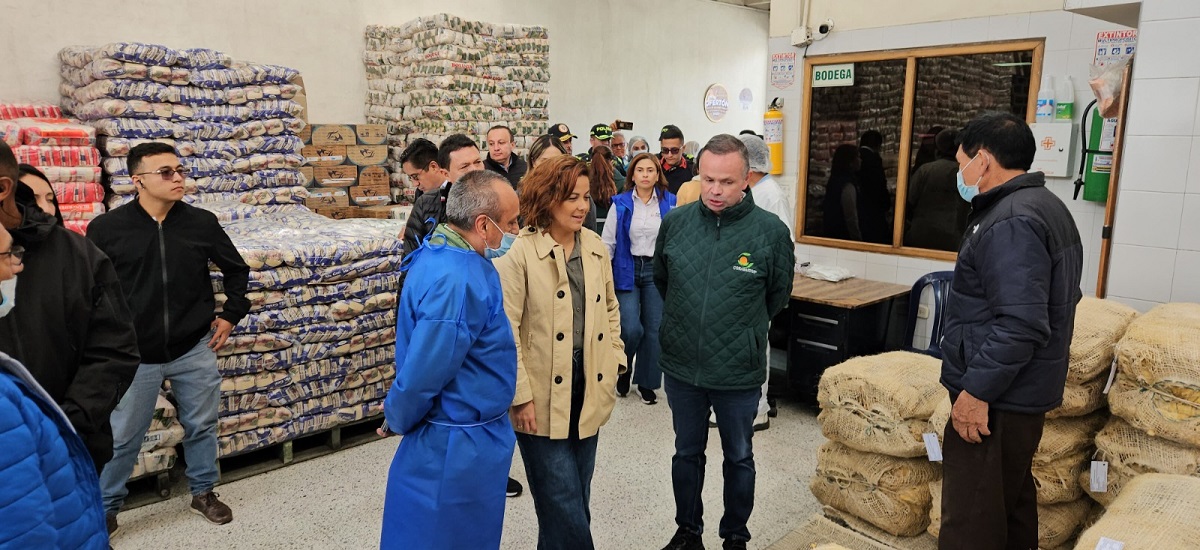 En la imagen, hay un grupo de personas de pie en lo que parece ser un almacén o instalación de almacenamiento. Las personas están vestidas con diversos estilos de ropa, lo que sugiere un ambiente informal o de negocios. 
