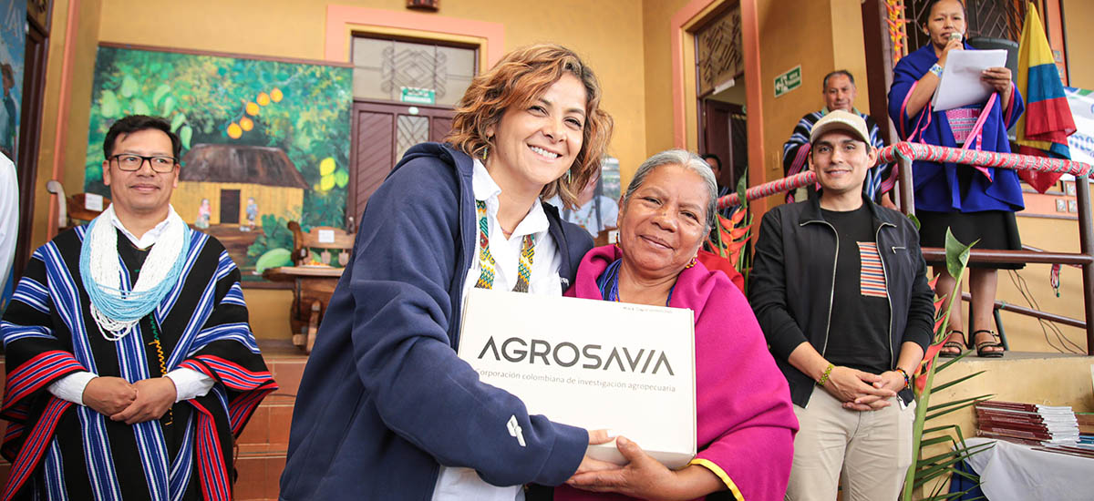 En la imagen se puede ver a la Ministra Jhenifer Mojica, la cual le esta entregando un reconocimiento a una señora, detrás se ven más personas participando del reconocimiento.