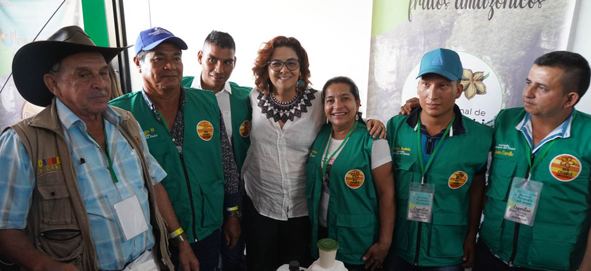 La imagen muestra a un grupo de personas que posan juntas para una foto. En total son seis personas, algunas de ellas con chalecos verdes. Todos sonríen y parecen disfrutar del momento. El grupo está formado por hombres y mujeres, y algunos llevan corbata. Están muy cerca unos de otros, lo que crea una sensación de camaradería y unidad.