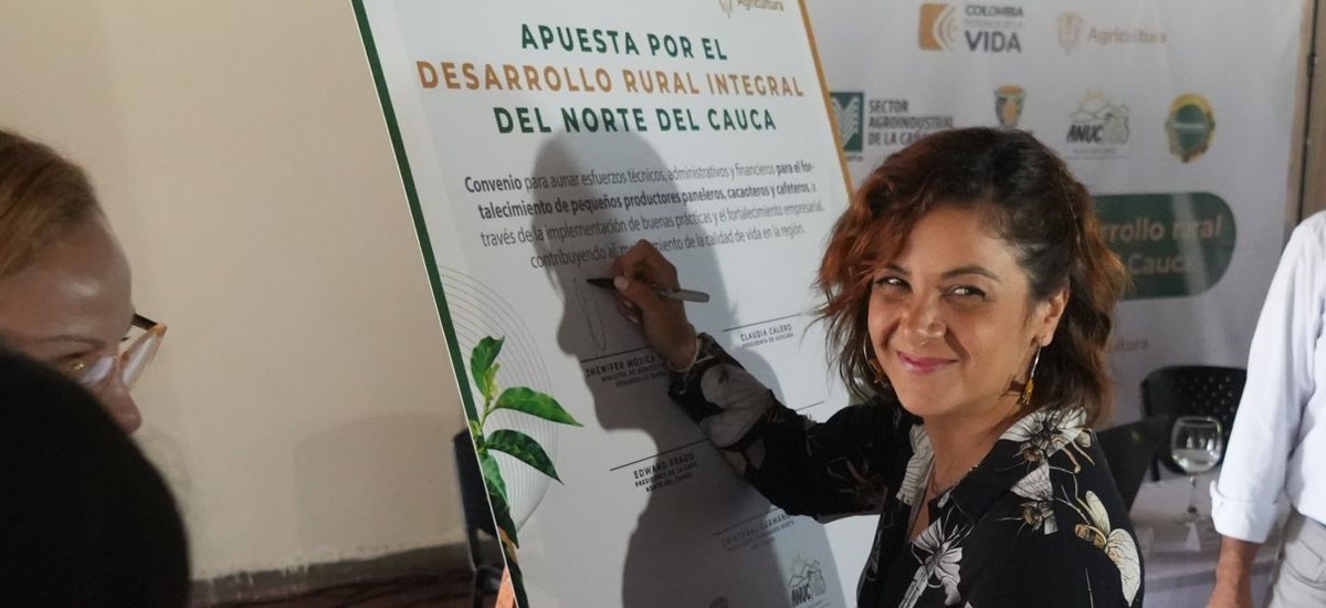 En la imagen se puede apreciar a la ministra Jhenifer Mojica, la cual esta sonriendo a la camara, mientras firma un cartel que dice "Apuesto por el desarrollo rural integral del norte del cauca"