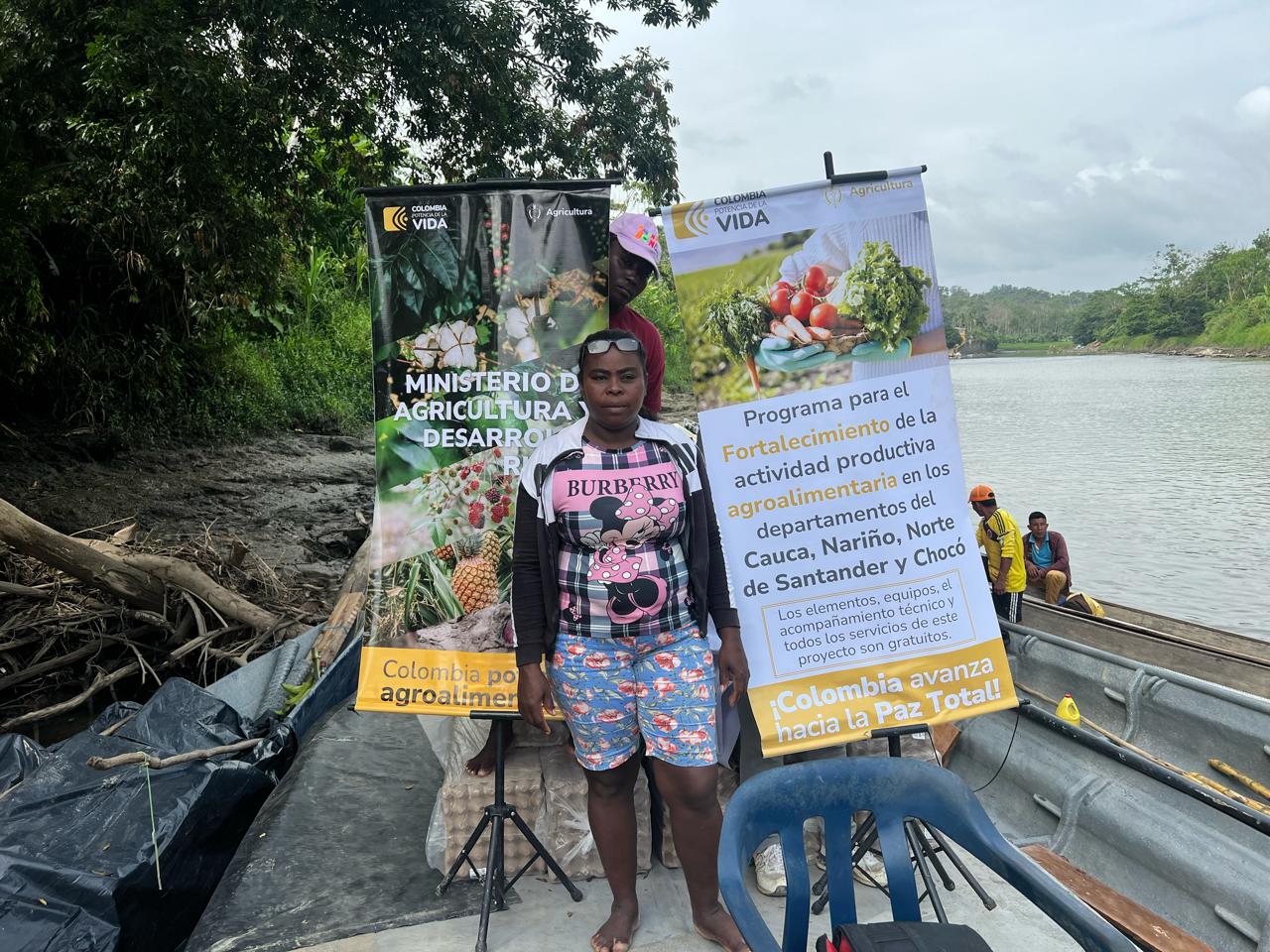 En la imagen aparece una persona de pie en un barco, sosteniendo un cartel que parece estar en español. El cartel menciona "Ministerio de Agricultura" y "Colombia", lo que indica que el evento o la iniciativa están relacionados con la agricultura en Colombia.