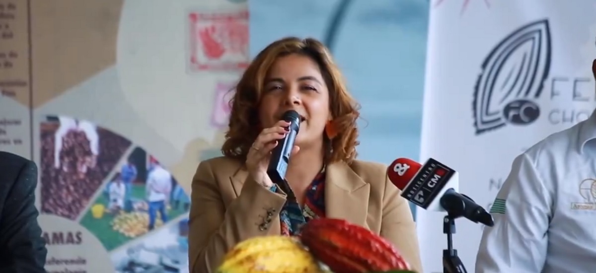 En la imagen aparece la ministra Jhenifer Mojica de pie ante un podio, hablando por un micrófono. Parece estar dirigiéndose a un público o participando en una rueda de prensa.