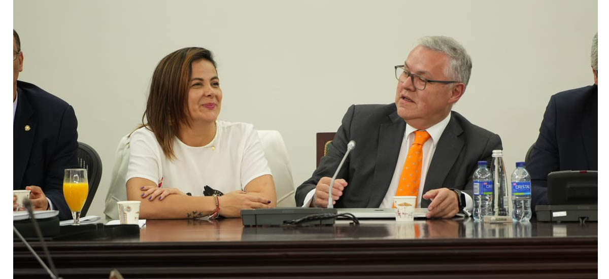 En la imagen se puede observar a la Ministra Jhenifer Mojica, junto con otros tres hombres en una reunion, a la Ministra se le nota contenta, lo que le da a la foto un entorno positivo