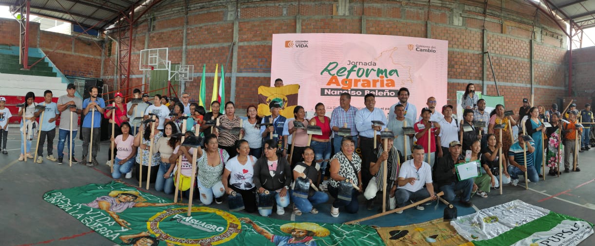 En la imagen se pueden ver muchas personas reunidas posando para una foto, de fondo se puede apreciar un cartel grande que dice, reforma agraria