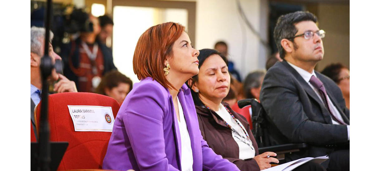 En la imagen se ve a tres personas sentadas en lo que parece ser un entorno formal o profesional. La persona en primer plano lleva una americana morada y mira hacia un lado con expresión pensativa. La persona del centro lleva una blusa blanca y tiene una expresión seria o contemplativa. La persona del fondo lleva un traje oscuro y también mira a un lado, posiblemente a algo o alguien que no se ve en la foto.  Traducción realizada con la versión gratuita del traductor DeepL.com