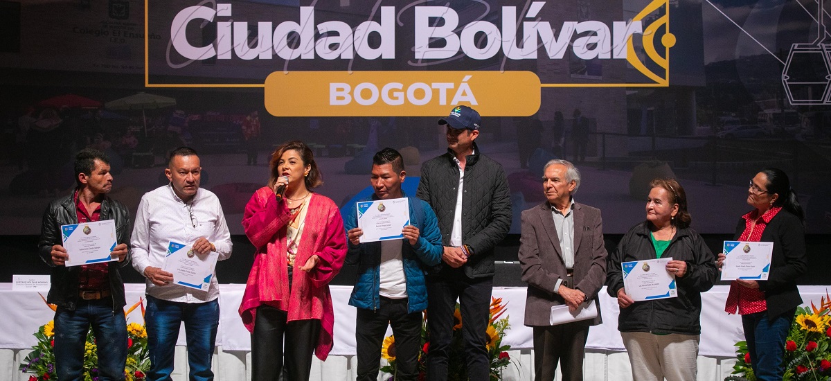 En la imagen se pueden observar a varias personas que sostienen lo que parece ser un diploma o reconocimiento y a la ministra Jhenifer Mojica hablando por el microfono, reconociendo a estas personas.