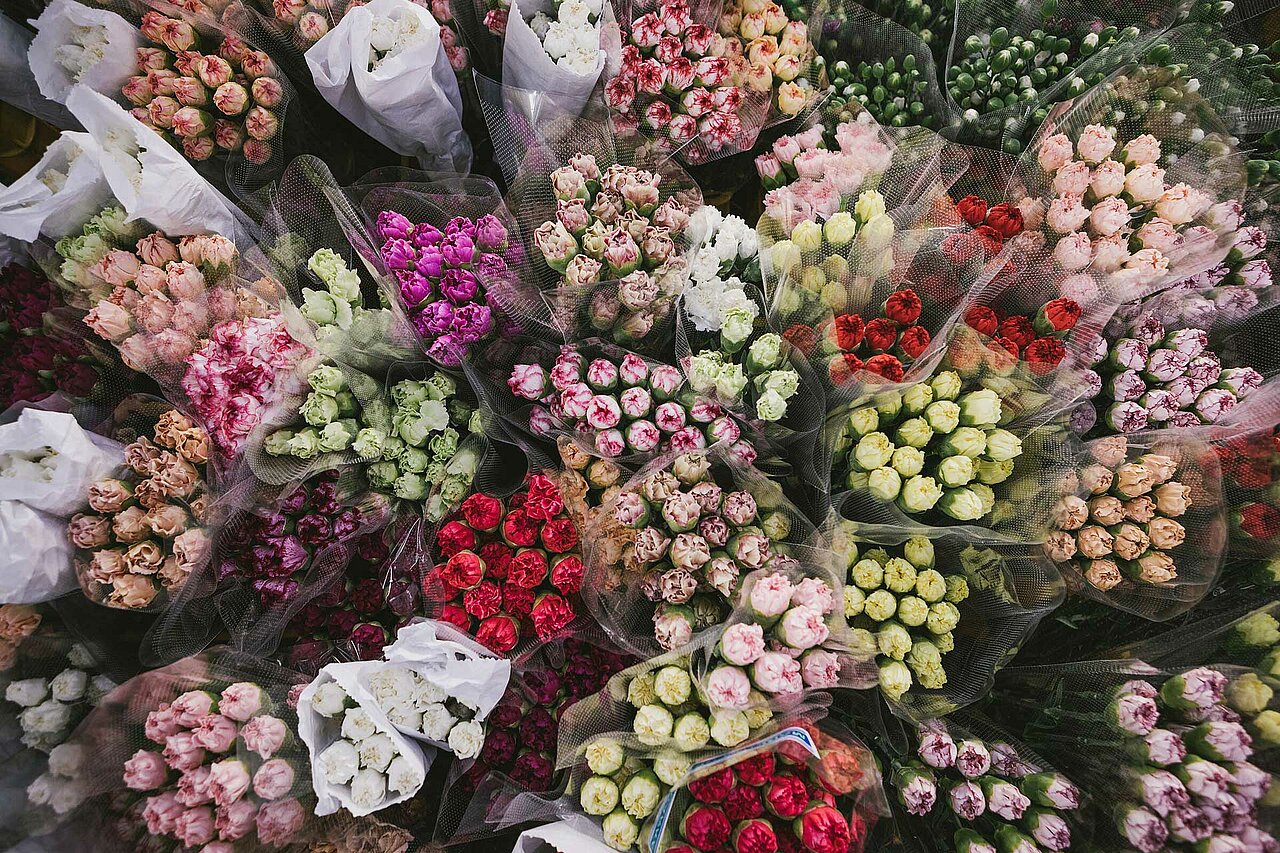 La imagen muestra un gran surtido de flores expuestas en varios jarrones y cestas. Las flores están dispuestas en forma circular, creando una presentación llamativa y visualmente atractiva. Los jarrones y las cestas están colocados sobre una mesa, y las flores son de distintos colores y tamaños, lo que añade belleza al conjunto. El arreglo crea una sensación de abundancia y variedad que lo convierte en un atractivo centro de mesa para cualquier evento o reunión.