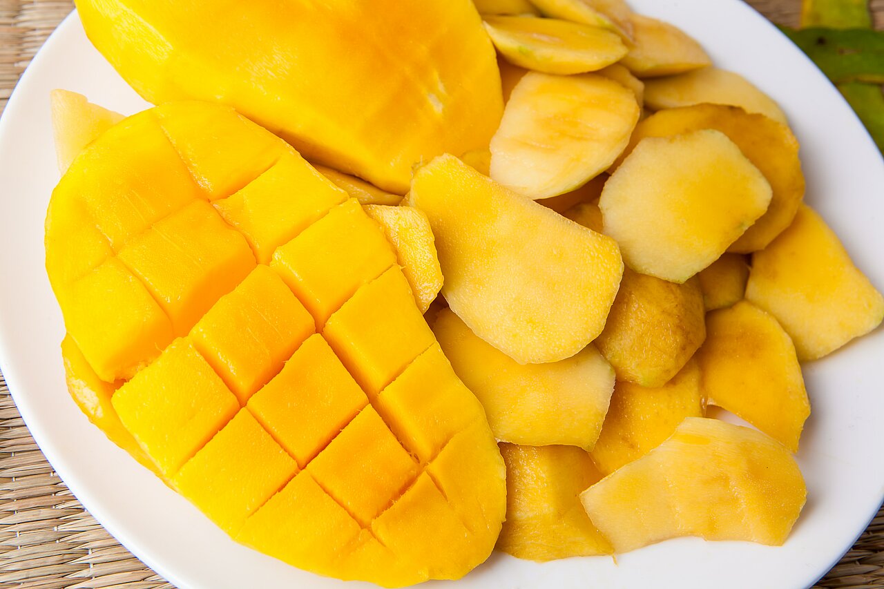La imagen muestra un plato blanco lleno de varios mangos cortados en rodajas. Los mangos están cortados en trozos y repartidos por el plato, algunos más grandes y otros más pequeños. 
