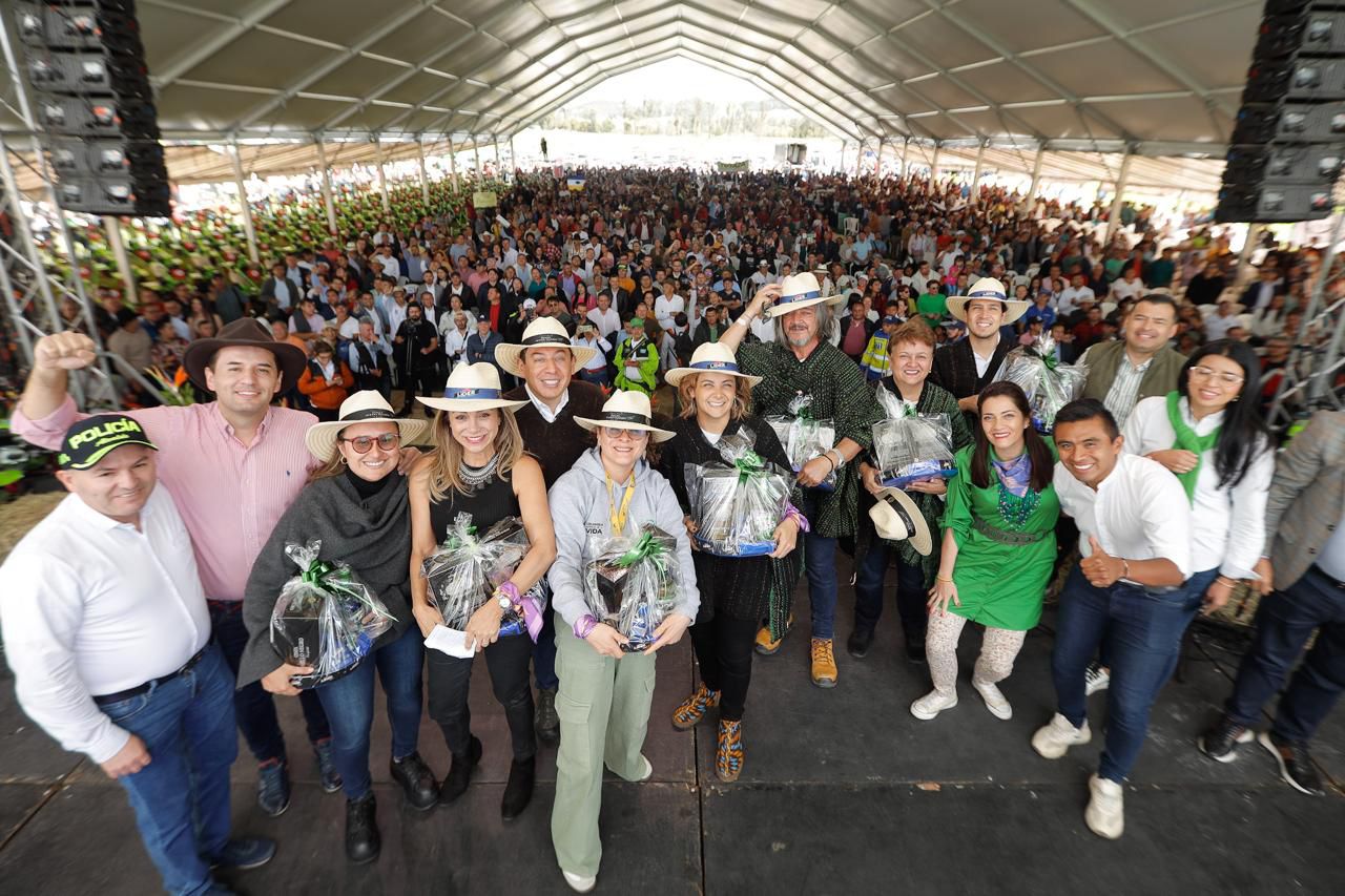 Esta es una imagen de un grupo de personas de pie en un escenario, probablemente en un evento o reunión. Van vestidos con una mezcla de ropa informal y semiformal, y algunos llevan sombrero.