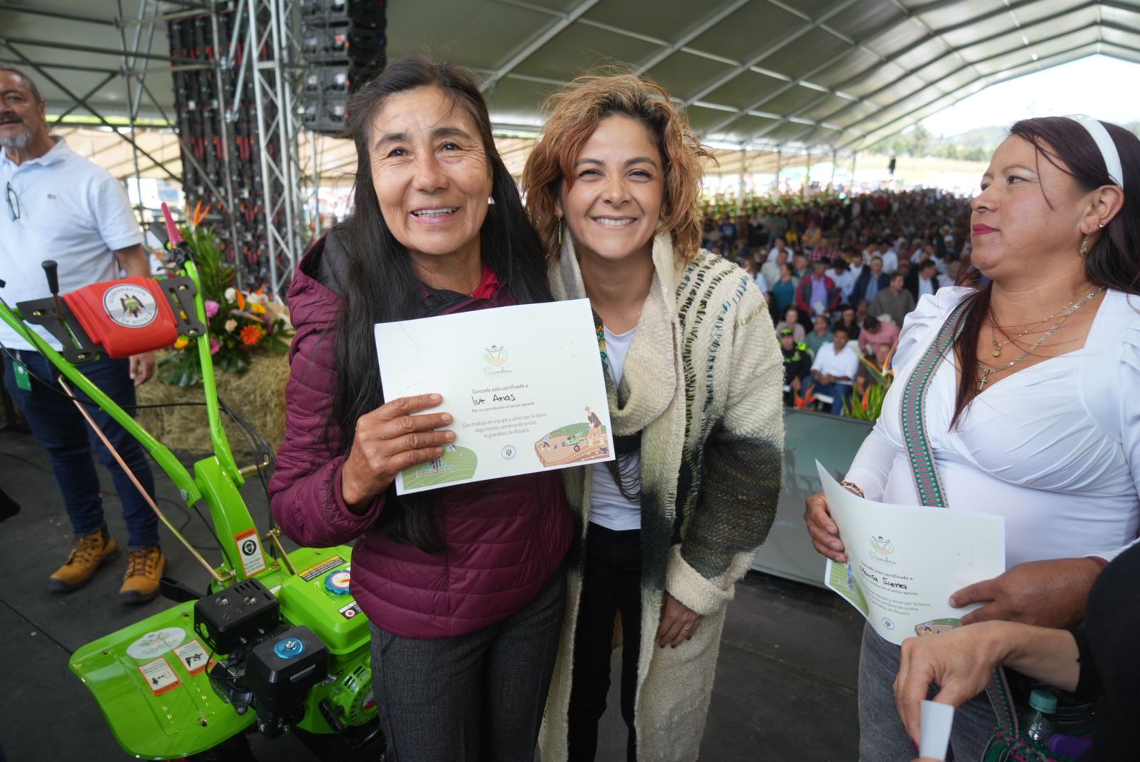  En la imagen aparecen tres mujeres juntas, sonrientes y sosteniendo lo que parecen ser certificados o premios. Están vestidas con ropa informal y una de ellas sostiene un objeto verde que podría ser un equipo o un elemento simbólico.