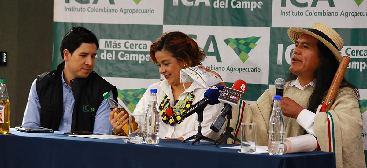 En la imagen se puede apreciar a tres personas, una de ellas es la ministra, parecen estar en una conferencia de prensa, una de las tres personas esta en un traje, mientras el otro hombre viste con una ruana y un sombrero.