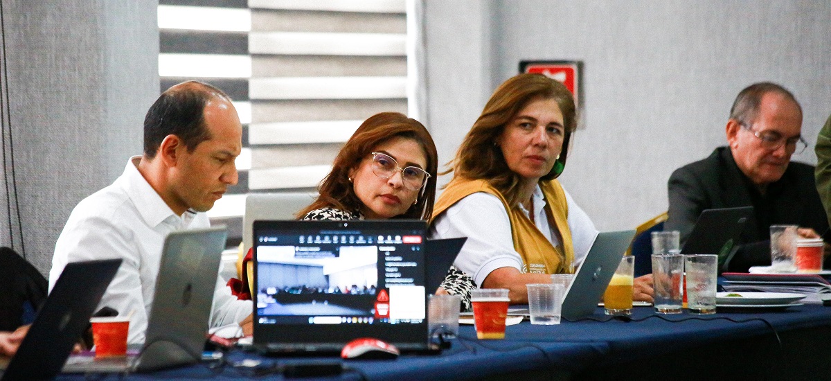 La imagen muestra a un grupo de personas sentadas alrededor de una mesa, participando en lo que parece ser una reunión o una conferencia. Están utilizando portátiles, lo que sugiere que podrían estar trabajando en un proyecto, discutiendo ideas o revisando documentos.