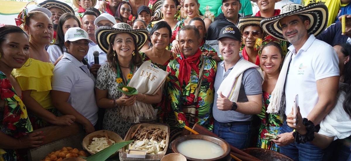 En la imagen se puede observar a un grupo de personas rodeando a la Ministra Jhenifer Mojica, a todos se les nota contentos en la imagen, frente a ellos, se puede observar algunos productos alimenticios.