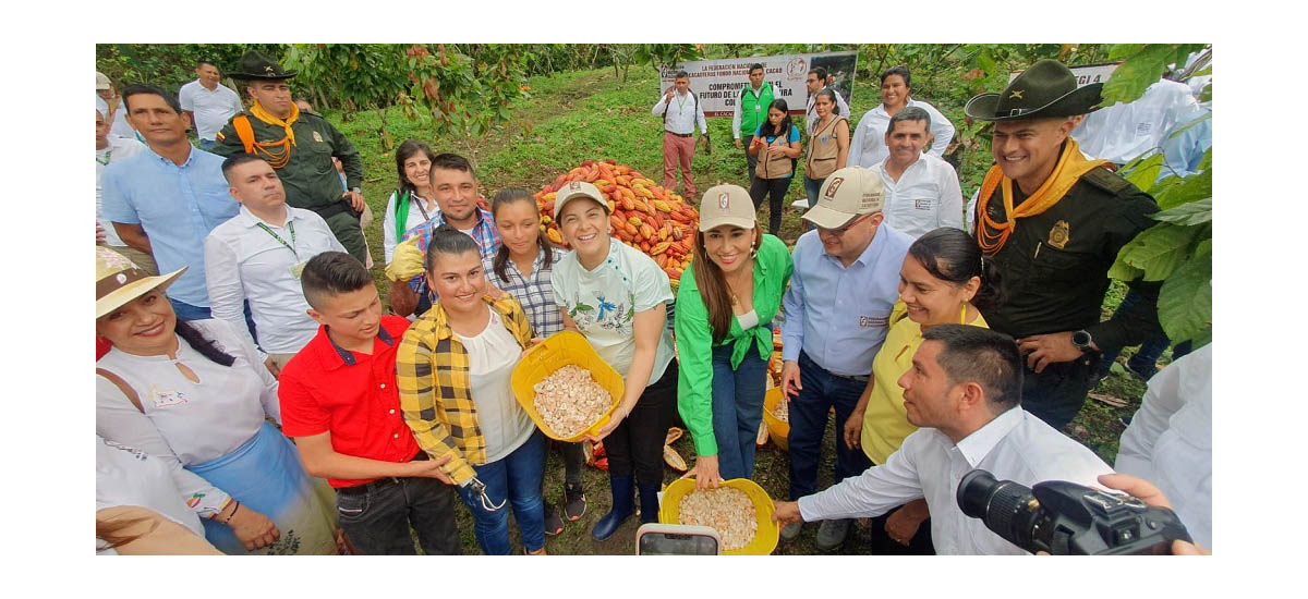 Esta imagen muestra a un grupo de personas reunidas al aire libre, posiblemente en una granja o evento agrícola. Sostienen bandejas amarillas con lo que parece ser un tipo de grano o semillas. Las personas sonríen y parecen posar para la foto, lo que indica un ambiente positivo y amistoso.