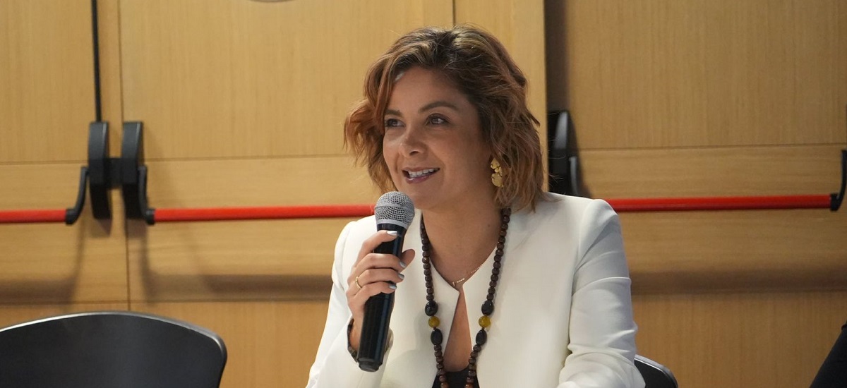 En la imagen se puede ver a la ministra Jhenifer Mojica, la cual se encuentra hablando por medio de un micrófono en lo que parece ser un evento, se le ve muy contenta.