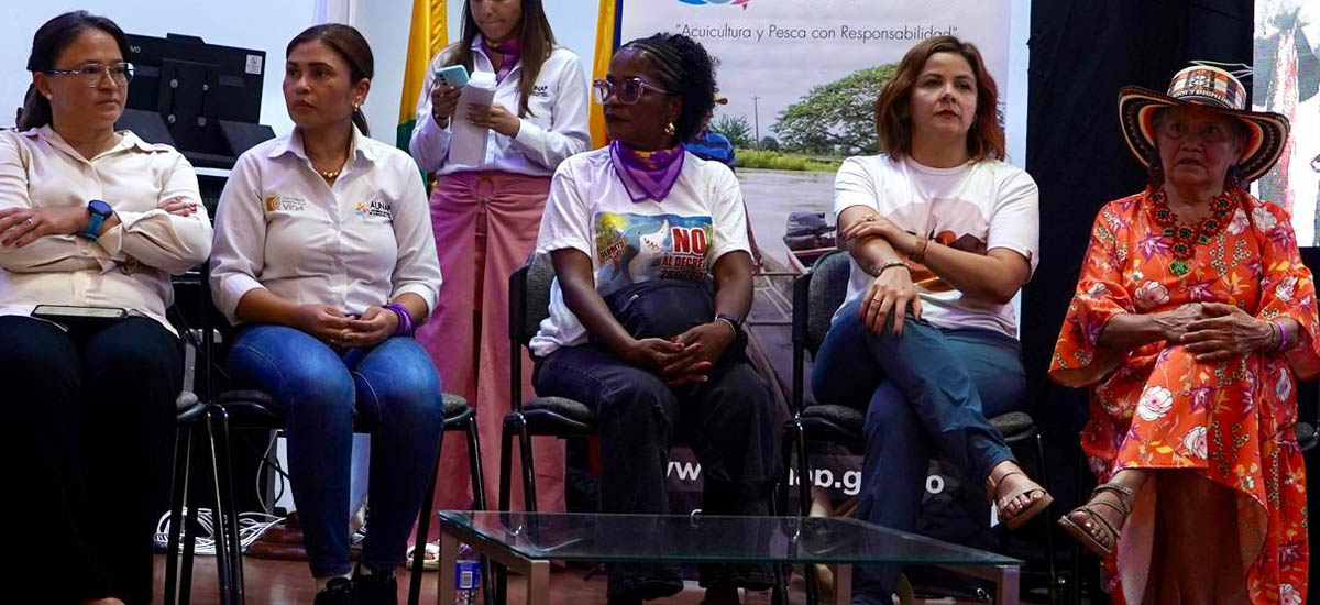 La imagen muestra a un grupo de personas sentadas en lo que parece ser una mesa redonda o una reunión. Se ven cinco personas, cada una con una postura y una expresión diferentes. Van vestidos con estilos variados, lo que sugiere que se trata de un acto informal o semiformal.