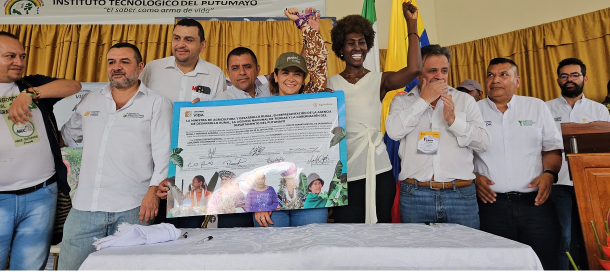 La imagen muestra a un grupo de personas reunidas en torno a una mesa, celebrando un acontecimiento o logro. Sostienen un gran documento o certificado, lo que sugiere que están recibiendo un premio o reconocimiento por su trabajo o sus logros.