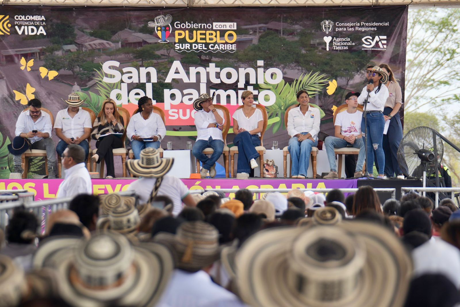 Esta imagen muestra la celebración de un acto público, probablemente en un entorno rural o semirrural, dada la presencia de una gran multitud y el ambiente informal.