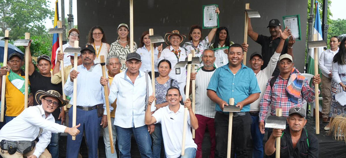 En la imagen se pueden ver muchas personas reunidas posando para una foto, de fondo se puede apreciar un cartel grande que dice, reforma agraria