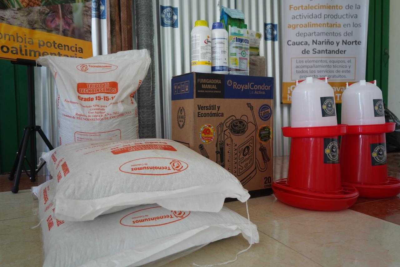 La imagen muestra una colección de productos y suministros agrícolas. También hay varias botellas, que podrían ser pesticidas, herbicidas u otros productos químicos agrícolas. El envase sugiere que estos productos están destinados a su uso en agricultura o jardinería. El entorno parece un almacén o una tienda donde se guardan o venden estos productos.